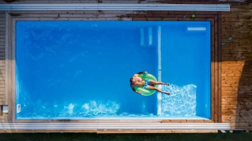 Aerial view of man lying in water in a backyardswimming pool outdoors.