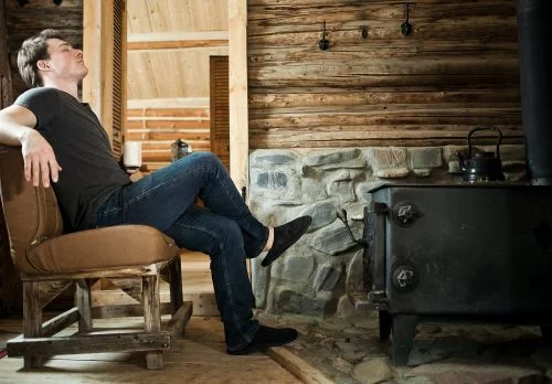 Man Relaxing in a cabin in front of a wood burning stove at peace with his home insurance rates